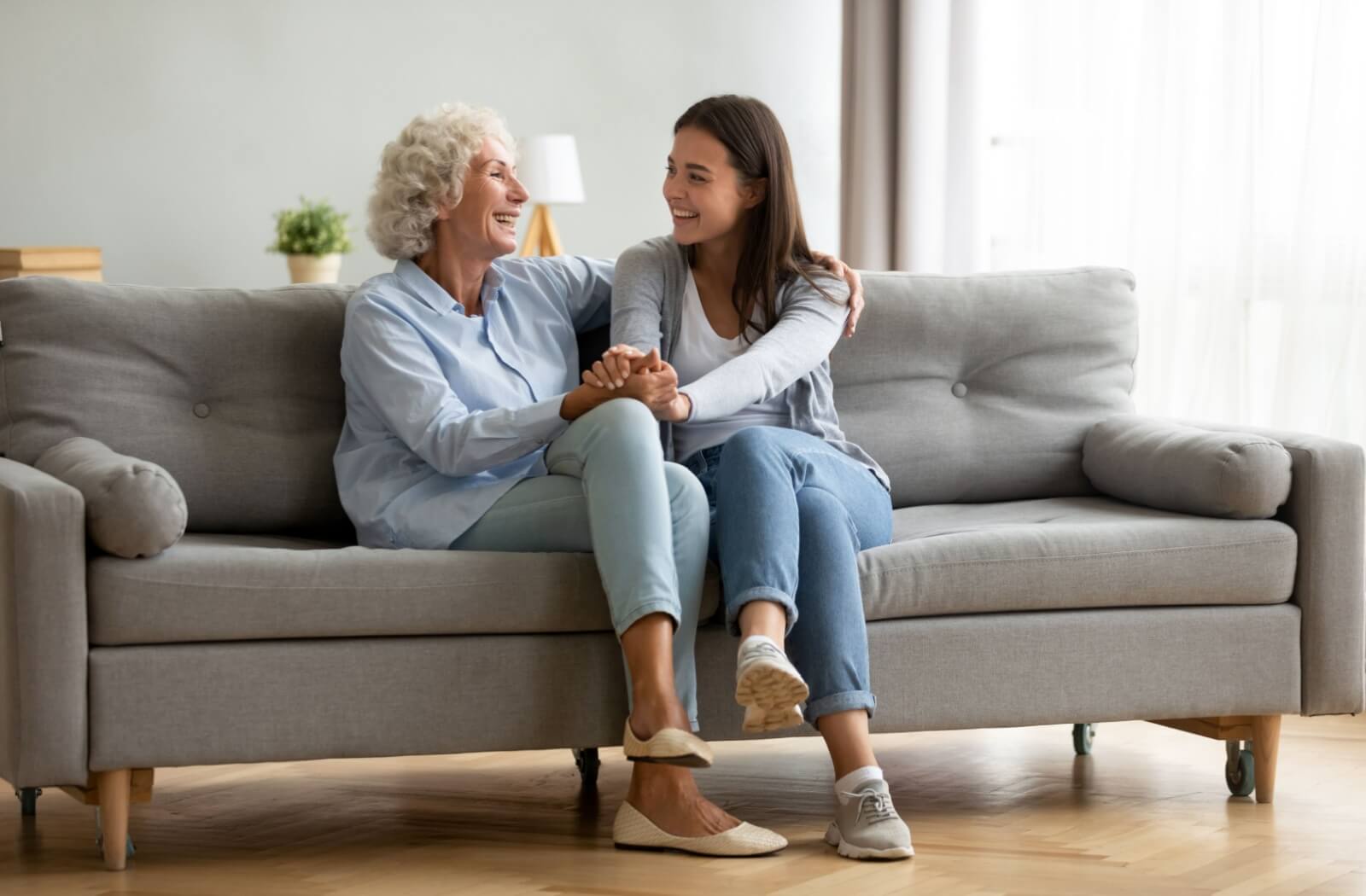 A senior parent and their adult child reminisce while sitting on a grey sofa.