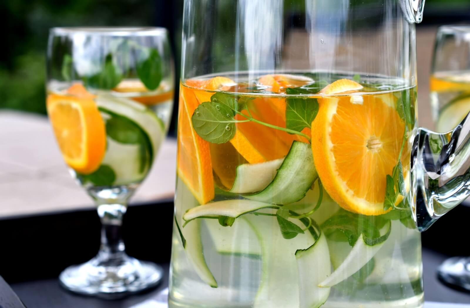 A pitcher of water with cucumber and orange in it.