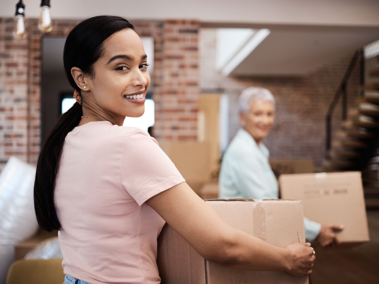 Smiling person wearing a pink t-shirt helping older adult pack cardboard boxes during move