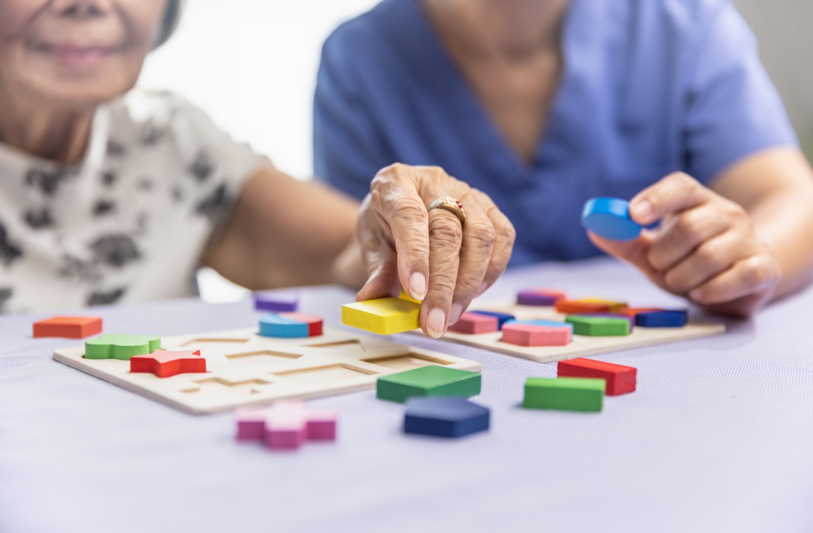 An older adult and their caregiver in memory care working together to complete a colored block puzzle.