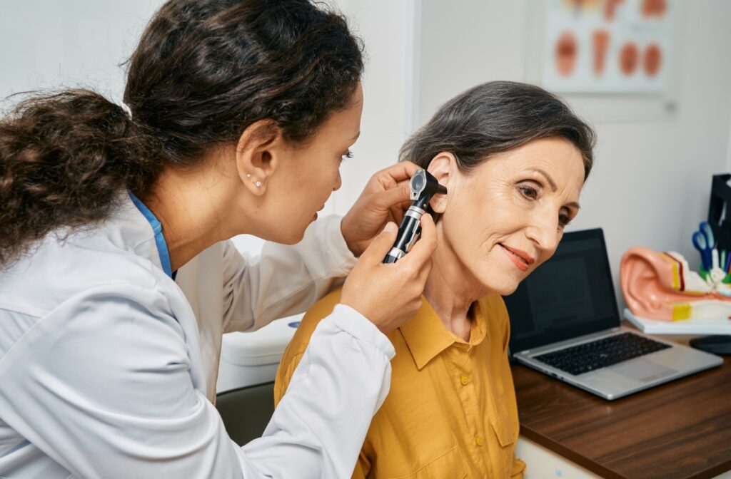 An older adult sits patiently while an audiologist examines their inner ear as part of a hearing loss evaluation