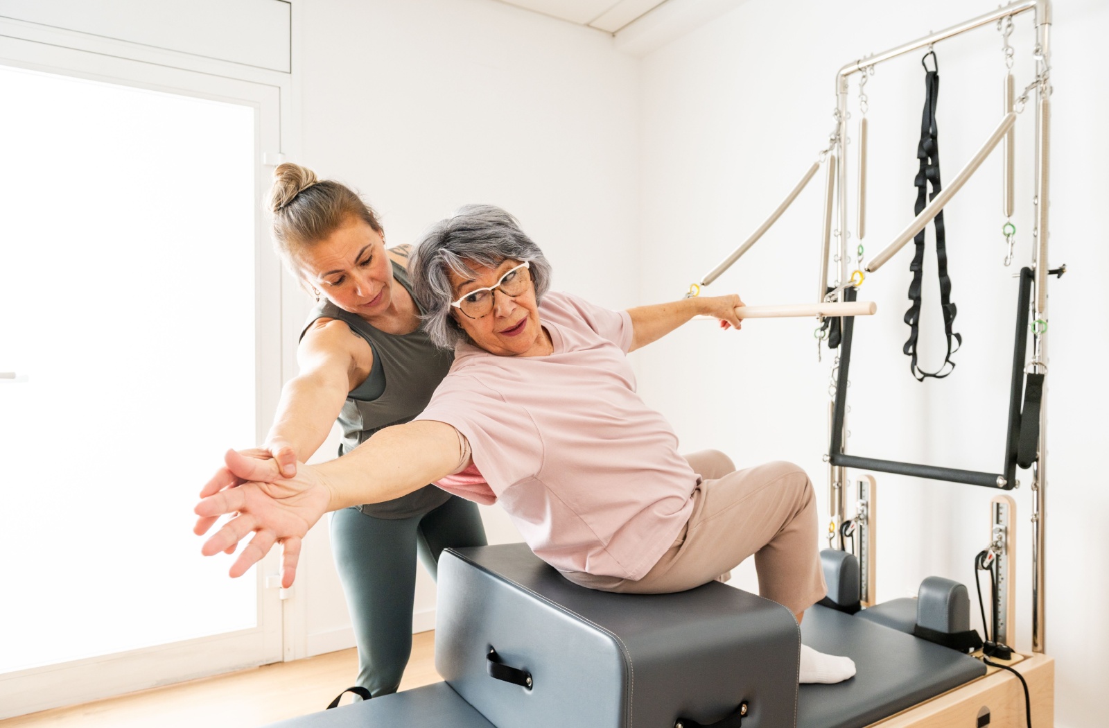 A fitness instructor gives a senior personalized training to practice Pilates moves to increase flexibility and balance