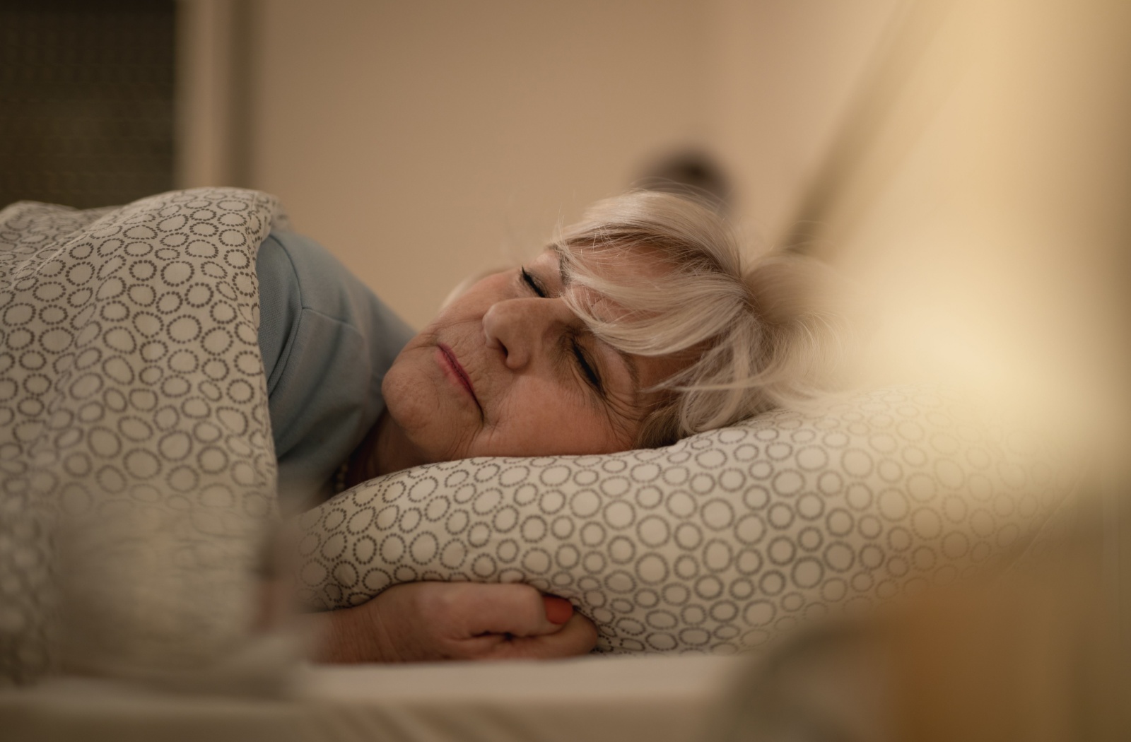 An older adult sleeps contently in a warm and well-lit room in their apartment in senior living