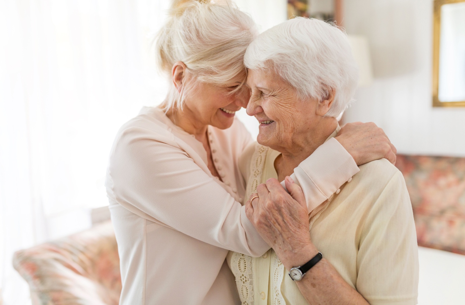 An adult child and their parent in memory care embrace and smile together