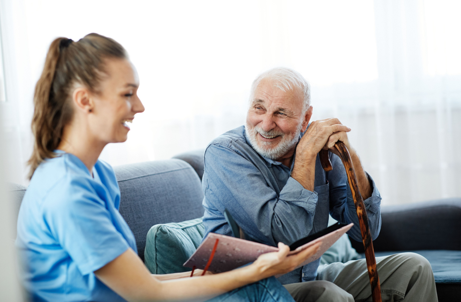 A senior in memory care smiles at a nearby caregiver while leaning on a cane