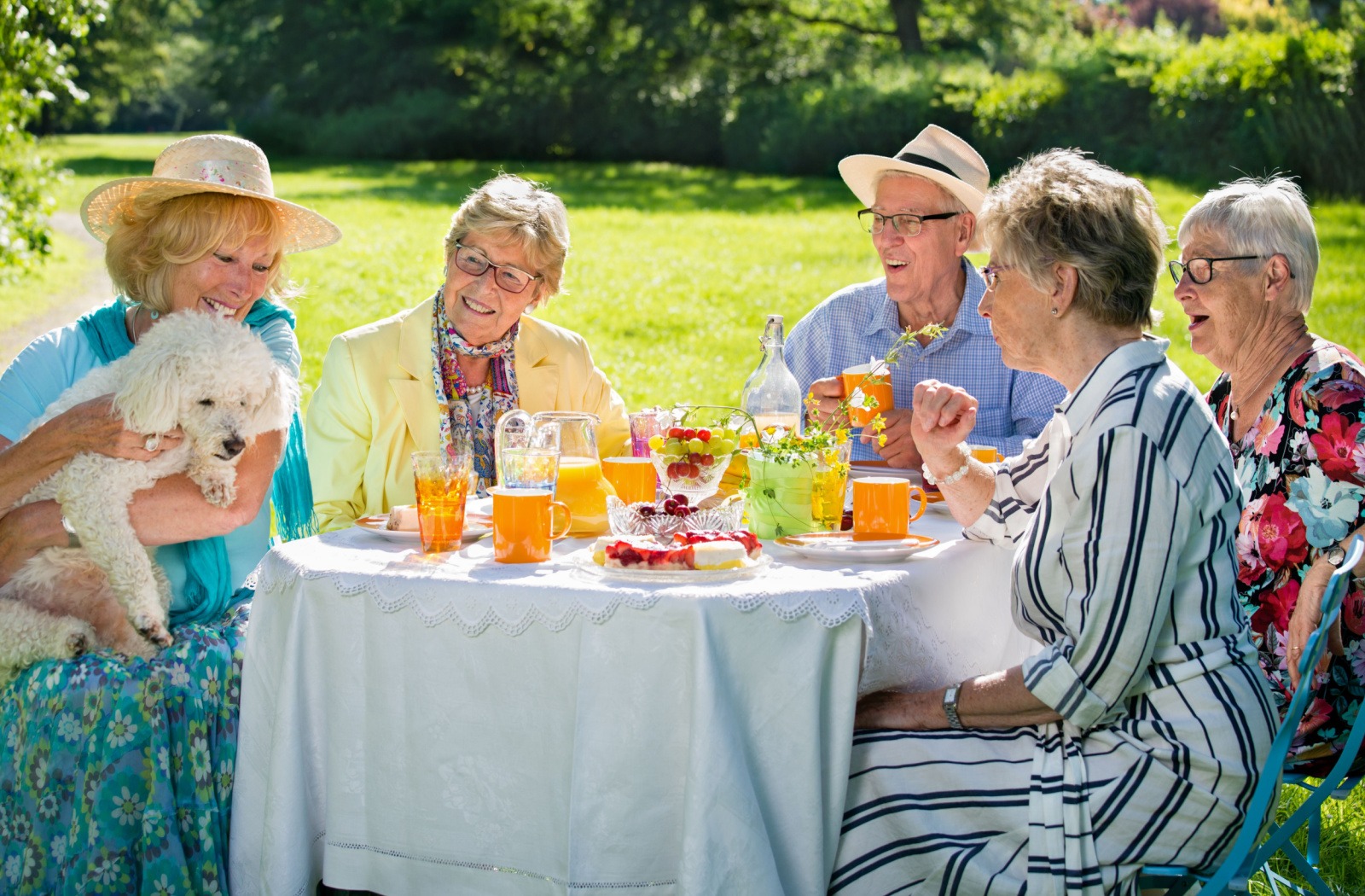 A group of seniors enjoy breakfast together outside, as one senior holds their pet dog on their lap.
