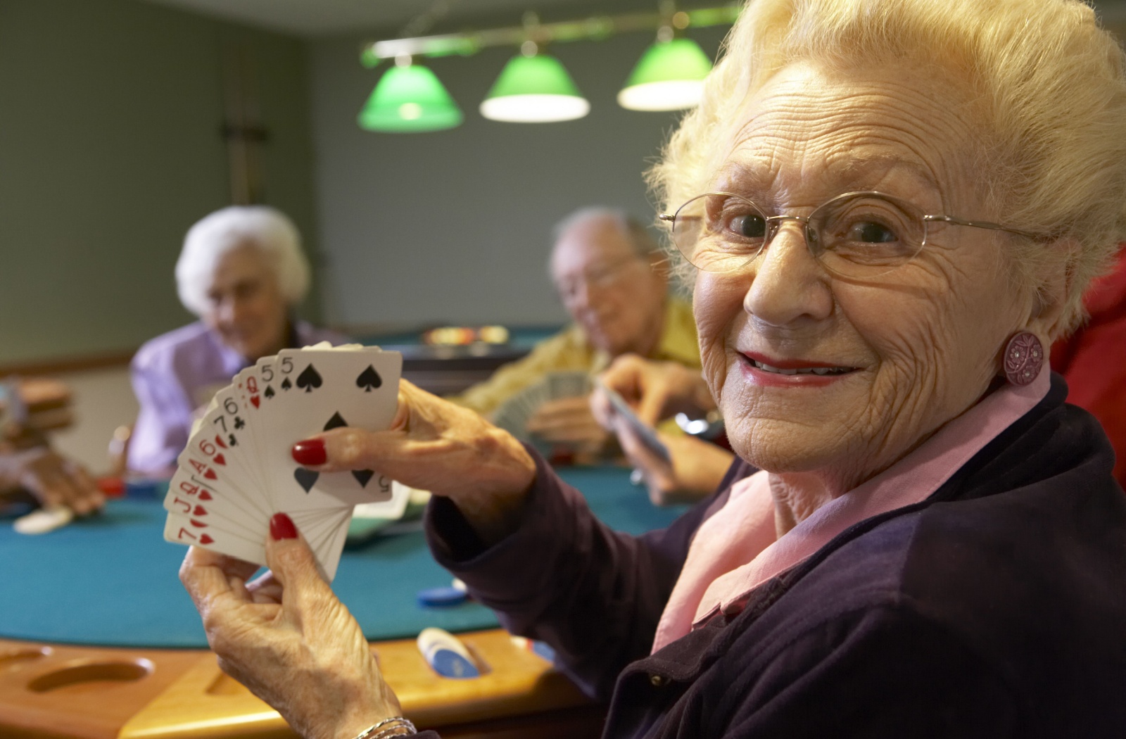 A senior shows their hand to the camera and smiles while playing a card game with friends.