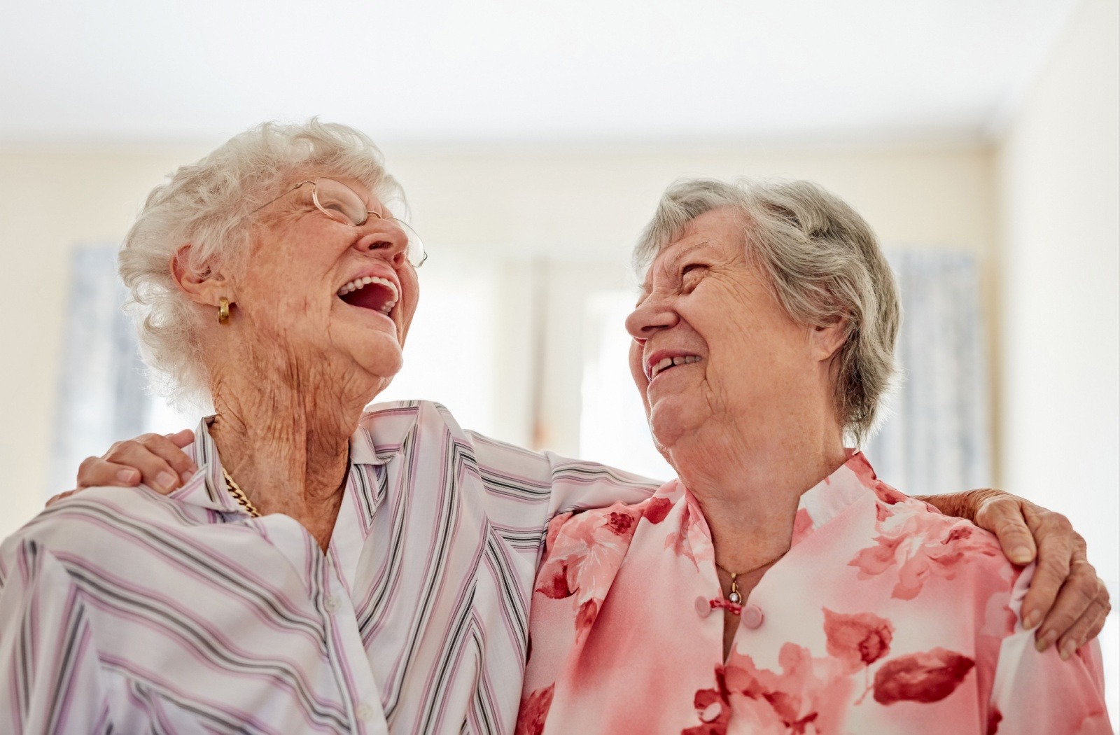 Two senior friends embrace each other and laugh together
