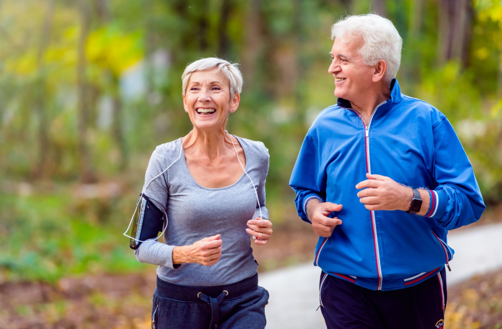 Two seniors go for a slow jog in a park.