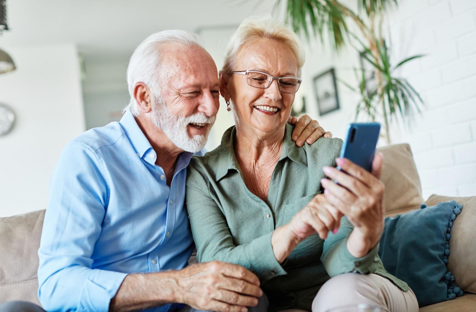 A senior couple smile as they video chat with a loved one from their smartphone