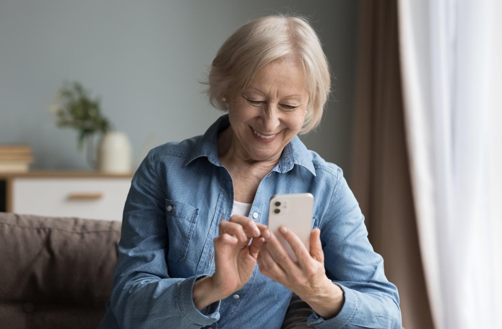 A senior smiles as they use a social media app on their smartphone.