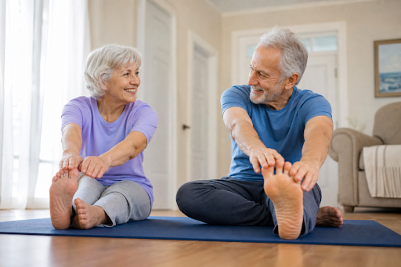 Two older adults smiling, doing seated forward stretches on yoga mats at home.